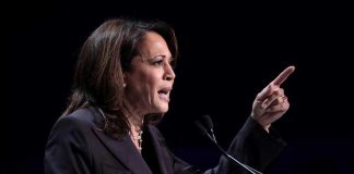 Person speaking at podium with raised finger.