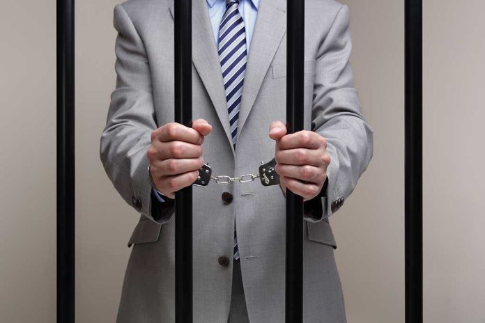shutterstock_136074335.jpg Businessman in a suit holding prison bars with handcuffs on his wrists
