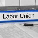 A black binder labeled Labor Union placed on a desk with papers and a pen