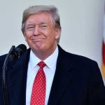 Trump REVIVES Biden Project – Finishing the Job! Man in suit and tie speaking at podium.