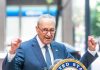 Man in suit and glasses speaks passionately at podium.