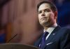 Rubio Unleashes Axe on State Dept – Makes Cuts! Man in suit speaking at podium.