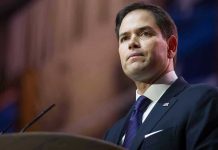 Rubio Unleashes Axe on State Dept – Makes Cuts! Man in suit speaking at podium.