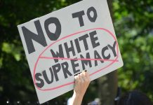 Campus ERUPTS – BIZARRE Nazi Uniform Attack! Sign saying No to white supremacy with red circle.