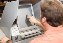 Person using touchscreen voting machine in polling booth.