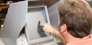 Person using touchscreen voting machine in polling booth.
