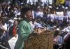 A woman passionately speaking at a political rally in front of a large crowd