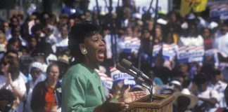 A woman passionately speaking at a political rally in front of a large crowd