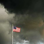 Terrifying Tornado Blitz – 50 Million Face Impact! American flag waving against a dark, stormy sky