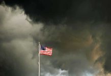 American flag waving against a dark, stormy sky
