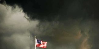 American flag waving against a dark, stormy sky