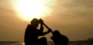 Silhouette of a guitarist sitting by the ocean during sunset