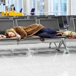 A traveler sleeping on a bench in an airport waiting area