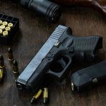 Handgun with ammunition, magazine, and rifle on wooden table.