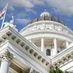 Capitol building dome and flags under a blue sky.