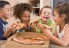 Four children joyfully sharing slices of pizza around a box