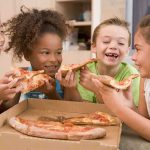 Four children joyfully sharing slices of pizza around a box