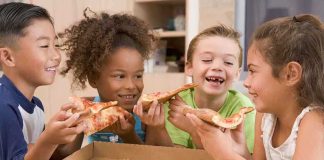 Four children joyfully sharing slices of pizza around a box