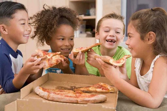 shutterstock_15488149.jpg Four children joyfully sharing slices of pizza around a box