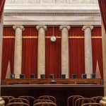Empty courtroom with columns, red curtains, and chairs.