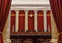 Empty courtroom with columns, red curtains, and chairs.