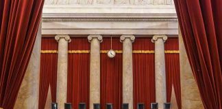 Empty courtroom with columns, red curtains, and chairs.