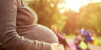 Pregnant woman sitting on a bench in a park during sunset