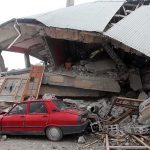 A red car parked next to a collapsed building with debris scattered around