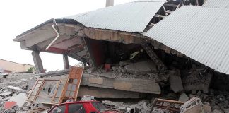 A red car parked next to a collapsed building with debris scattered around