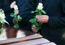 Mourners holding white roses by a casket.