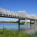 A large metal bridge spanning over a river with a clear blue sky in the background