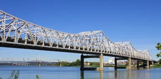 A large metal bridge spanning over a river with a clear blue sky in the background