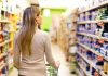 A woman pushing a shopping cart in a supermarket aisle filled with products