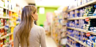 A woman pushing a shopping cart in a supermarket aisle filled with products