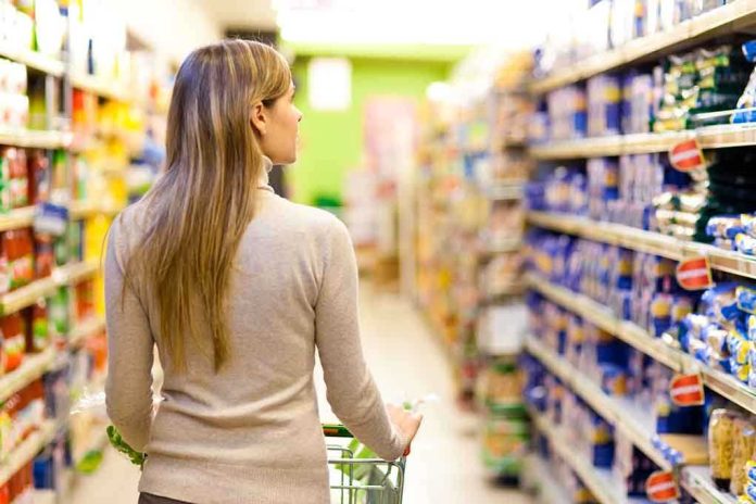 A woman pushing a shopping cart in a supermarket aisle filled with products