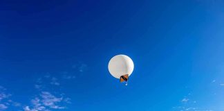 A white balloon floating in a clear blue sky with scattered clouds