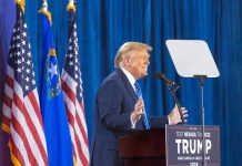 Trump’s AI Ban Stuns Nation Person speaking at podium with flags in background.