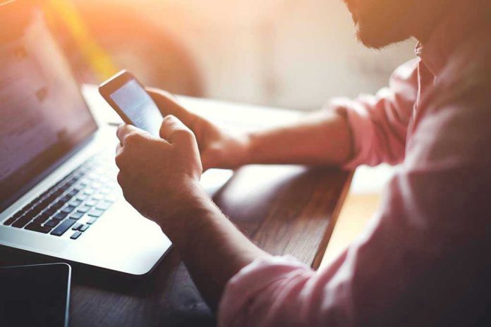 Person using a smartphone and laptop at desk.