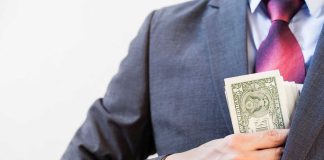 Person in suit putting dollars in jacket pocket.