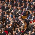 Audience of officials sitting and reading documents in auditorium.