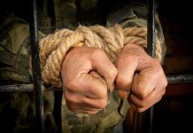 Hands tied with rope gripping prison bars