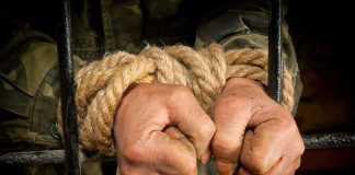 Hands tied with rope gripping prison bars