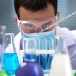 Scientist pipetting blue liquid into test tubes.