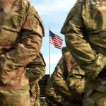 Promised Benefits REVOKED — Army Hit Hardest Soldiers stand in formation with American flag in background.
