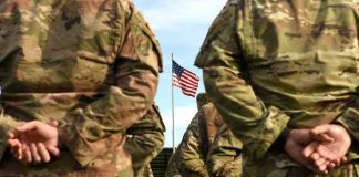 Soldiers stand in formation with American flag in background.