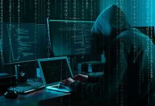 Hacker in dark room surrounded by computer screens.