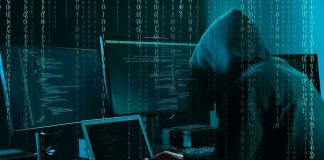 Hacker in dark room surrounded by computer screens.