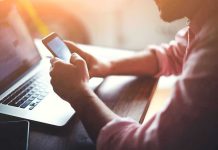 Person using a smartphone and laptop at desk.