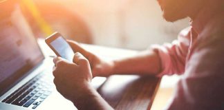 Person using a smartphone and laptop at desk.