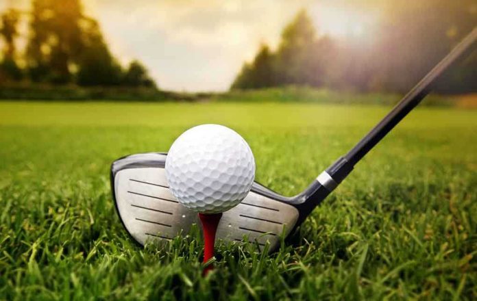 shutterstock_158881226.jpg A golf ball on a tee with a golf club resting beside it on green grass